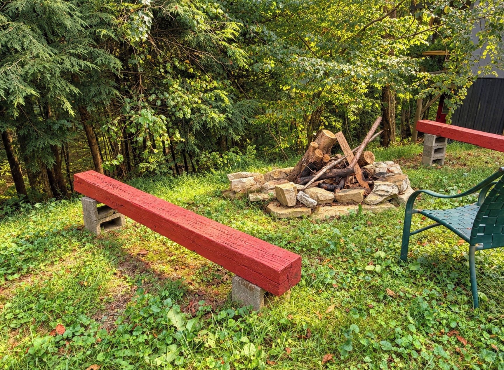 Un espace extérieur aménagé en harmonie avec la nature, avec un foyer entouré de rochers, deux bancs et un fauteuil vert.