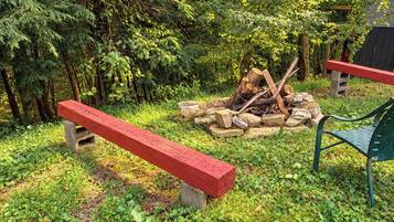 Un espace extérieur aménagé en harmonie avec la nature, avec un foyer entouré de rochers, deux bancs et un fauteuil vert.