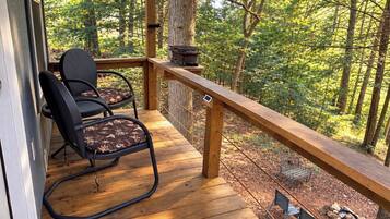 Une terrasse en bois avec deux chaises et une table, donnant sur une zone boisée.