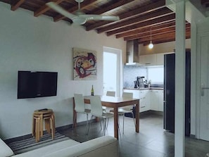 A modern living room with a flat-screen TV, a dining area with a table and chairs, and a kitchen with a stove and cabinets. - Restored fisherhouse for 6 persons (Lira (Santa Maria))