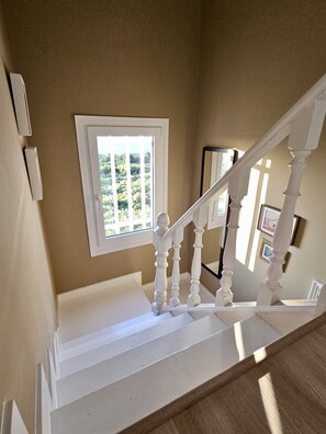 Eine Treppe mit weißen Spindeln, ein Fenster mit Blick auf Grünflächen und eine Tür mit Lichtschalter.