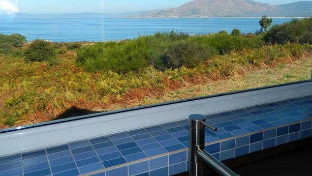 A view from a window with a metal railing, overlooking a coastal landscape with greenery and a body of water. - Restored fisherhouse for 6 persons (Lira (Santa Maria))