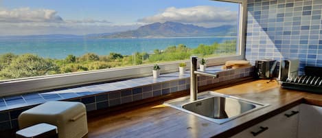 A kitchen with a view of the sea and mountains, a sink, a stove, and a window with a view.
