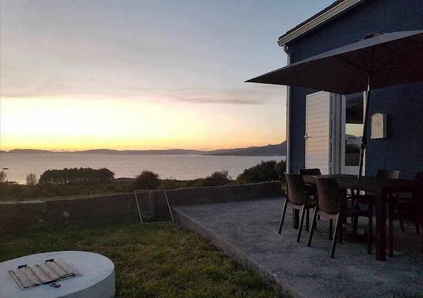 A patio with a view of the sea at sunset, a table with chairs, and a small round table with a mat. - Restored fisherhouse for 6 persons (Lira (Santa Maria))