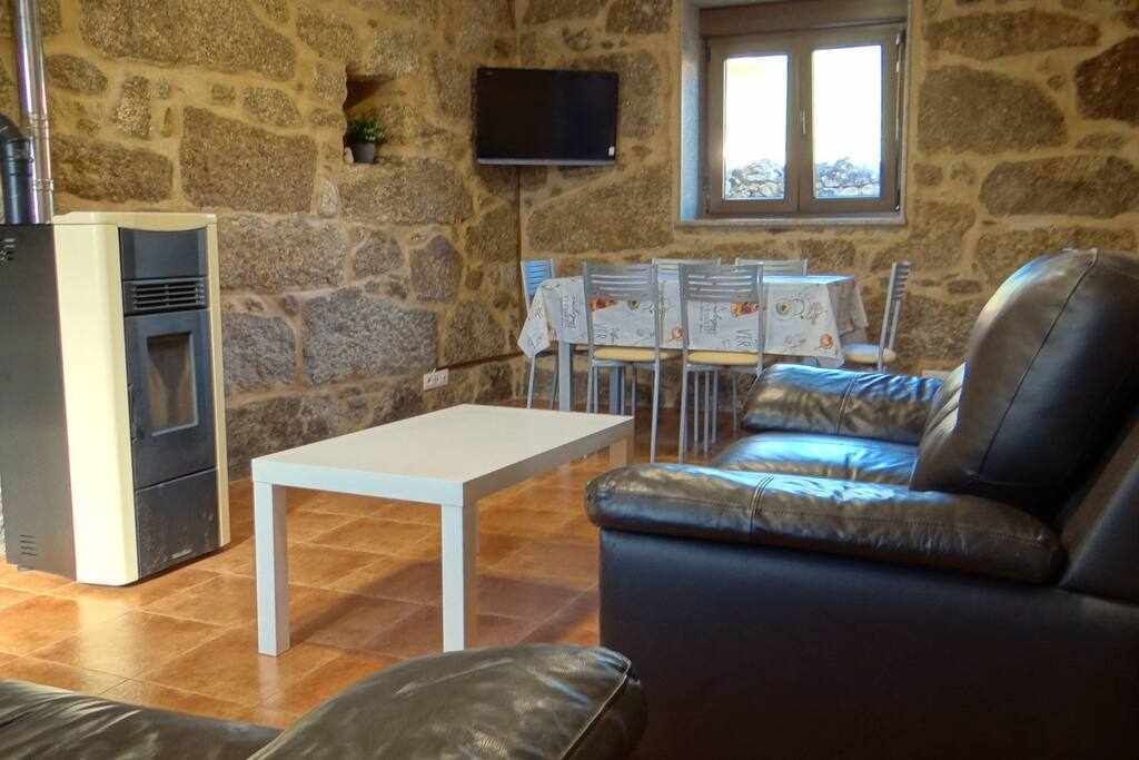 Una habitación de paredes de piedra con chimenea, un televisor montado en la pared, una mesa de comedor con sillas y un sofá de cuero.