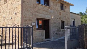 Un bâtiment en pierre doté d’une entrée fermée par un portail, d’un petit porche et d’une fenêtre ornée d’un rideau.