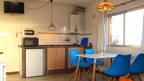Cuina compacta amb microones, nevera i un petit rentaplat. Zona de menjador amb cadires blaves i taula.