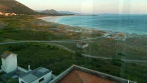 Paisatge costaner amb carretera cap a una platja, un edifici petit i muntanyes allunyades.