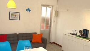 Habitació petita i lluminosa amb sofà, taula de dinar i petita cuina.