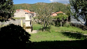 Entorno rural con casas de piedra, un pequeño huerto y una colina al fondo.