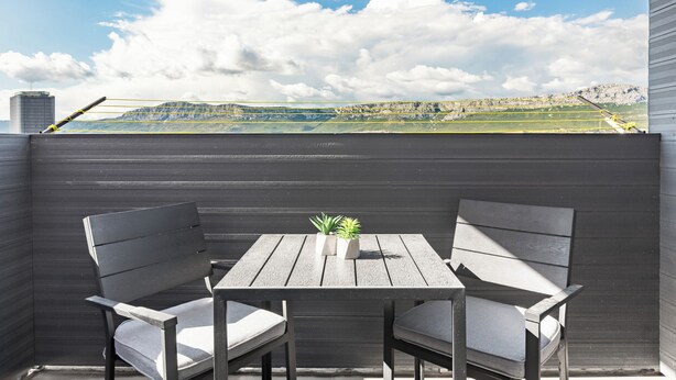 A wooden table with two chairs and two potted plants on a balcony with a view of a mountainous landscape. - Did' (Split)
