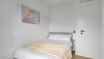 Une chambre à coucher avec un lit, un mur blanc, une porte et un tableau abstrait aux couleurs vives.