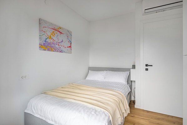 Une chambre à coucher avec un lit, un mur blanc, une porte et un tableau abstrait aux couleurs vives.