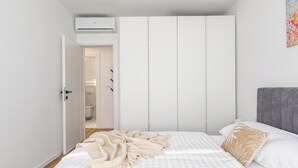 A bedroom with a bed, a grey headboard, a white wardrobe, and an air conditioning unit. - Did' (Split)