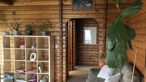 A cozy log cabin interior with a wooden bookshelf, a grey sofa, and a large potted plant. - Good Vibes Cabin - Car rental available! (Craig)