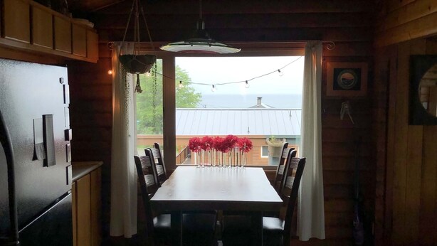 A wooden cabin interior with a dining table, chairs, a refrigerator, and a view of the outdoors. - Good Vibes Cabin - Car rental available! (Craig)