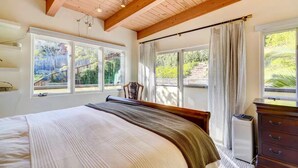 Ein Schlafzimmer mit einem großen Bett, Holzbalken an der Decke, einem Fenster mit Vorhängen und Blick auf Grünlandschaft.