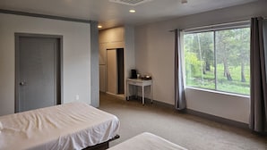 Ett hotellrum med en säng, ett skrivbord och ett fönster med utsikt över träd.