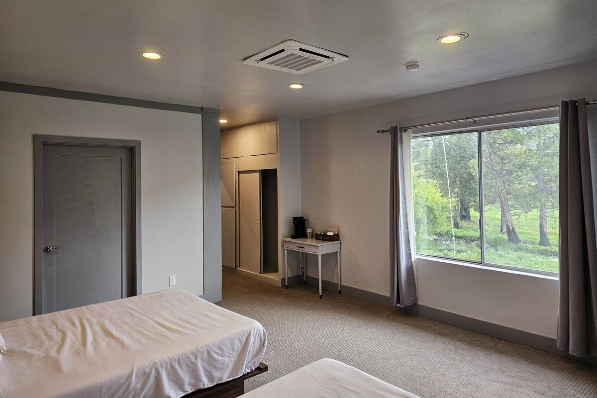 A hotel room with a bed, a desk, and a window with a view of trees.