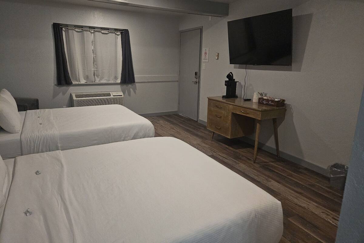 A hotel room with two single beds, a wooden desk, a flat-screen TV, and a window with curtains.