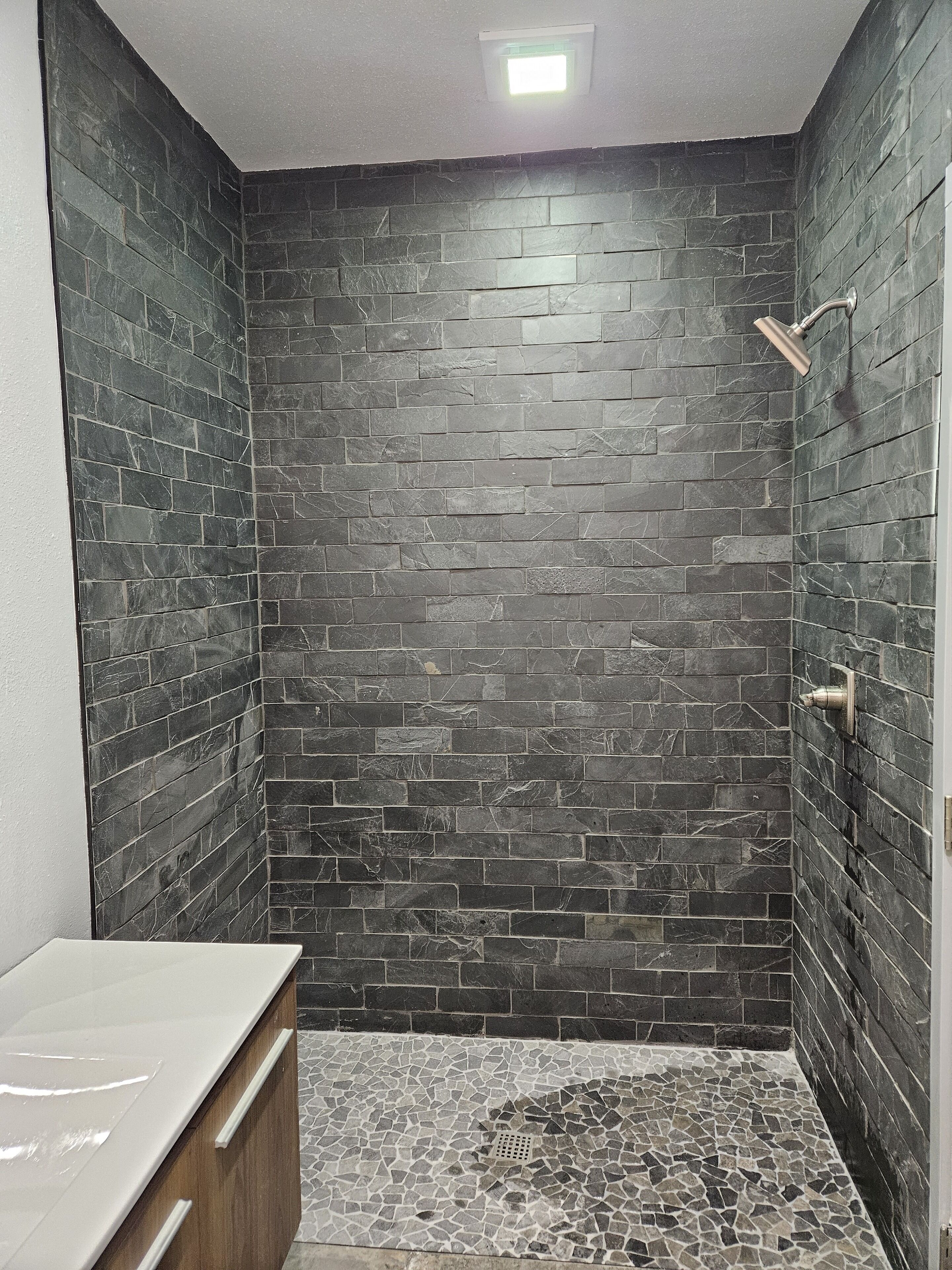 A shower with dark stone tiles and a mosaic floor.