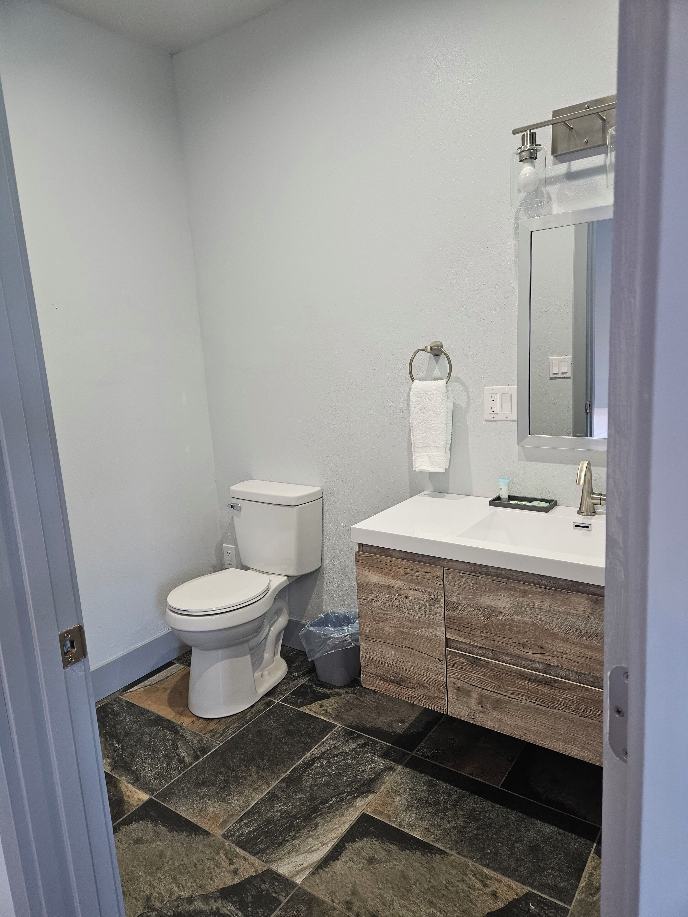 A bathroom with a white toilet, a sink with a mirror above it, and a trash bin.