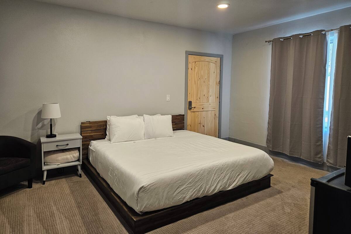 A bedroom with a bed, bedside table, lamp, and a door.