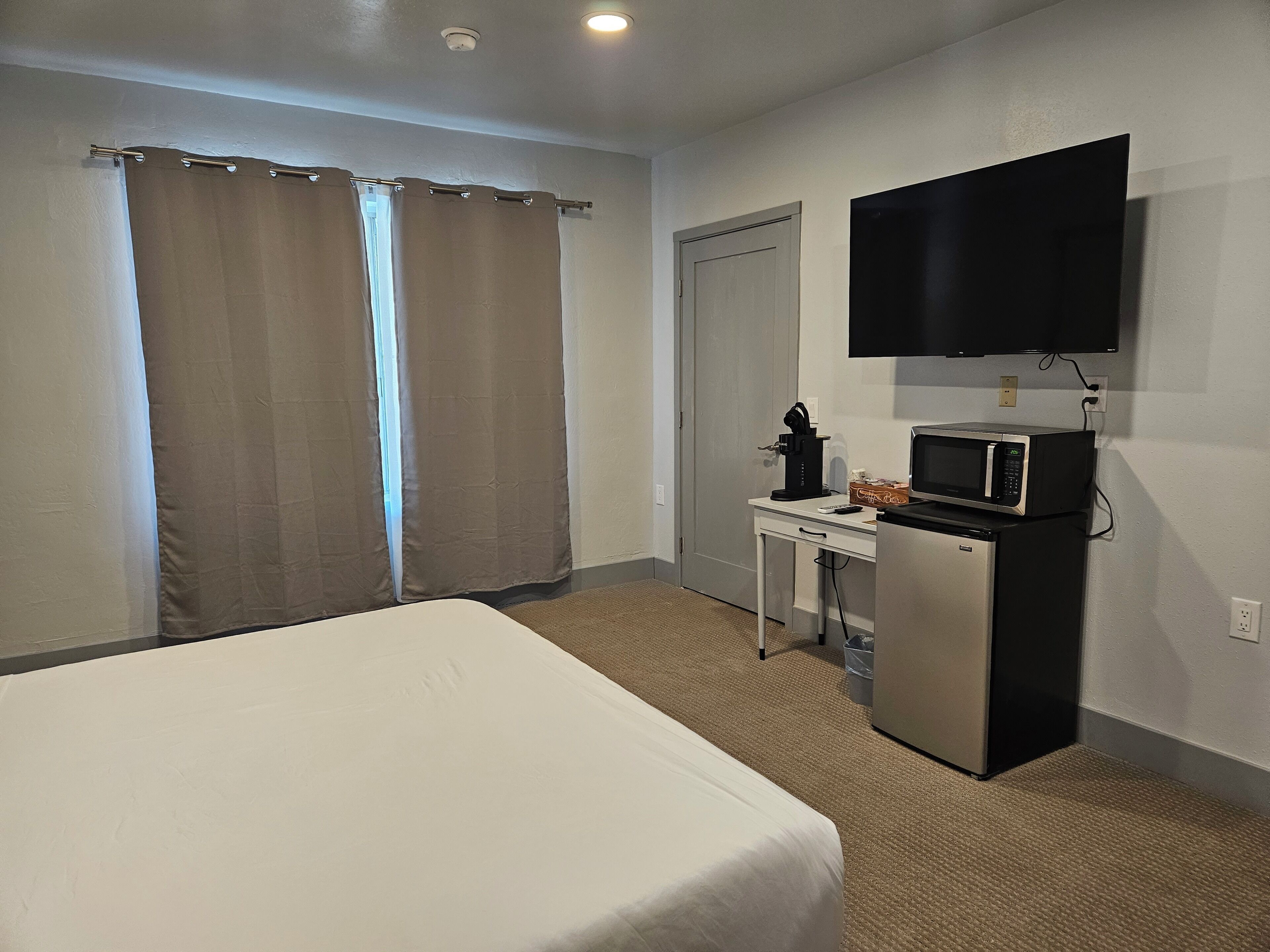 Una camera d'albergo con un letto, una scrivania con un forno a microonde, una TV e una porta.