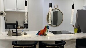 Cocina moderna con armarios blancos, encimera de mármol, taburetes negros y luces colgantes.