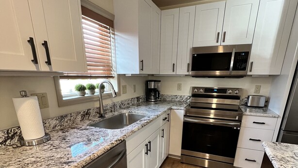 A modern kitchen with white cabinets, stainless steel appliances, a granite countertop, and a wooden floor.
