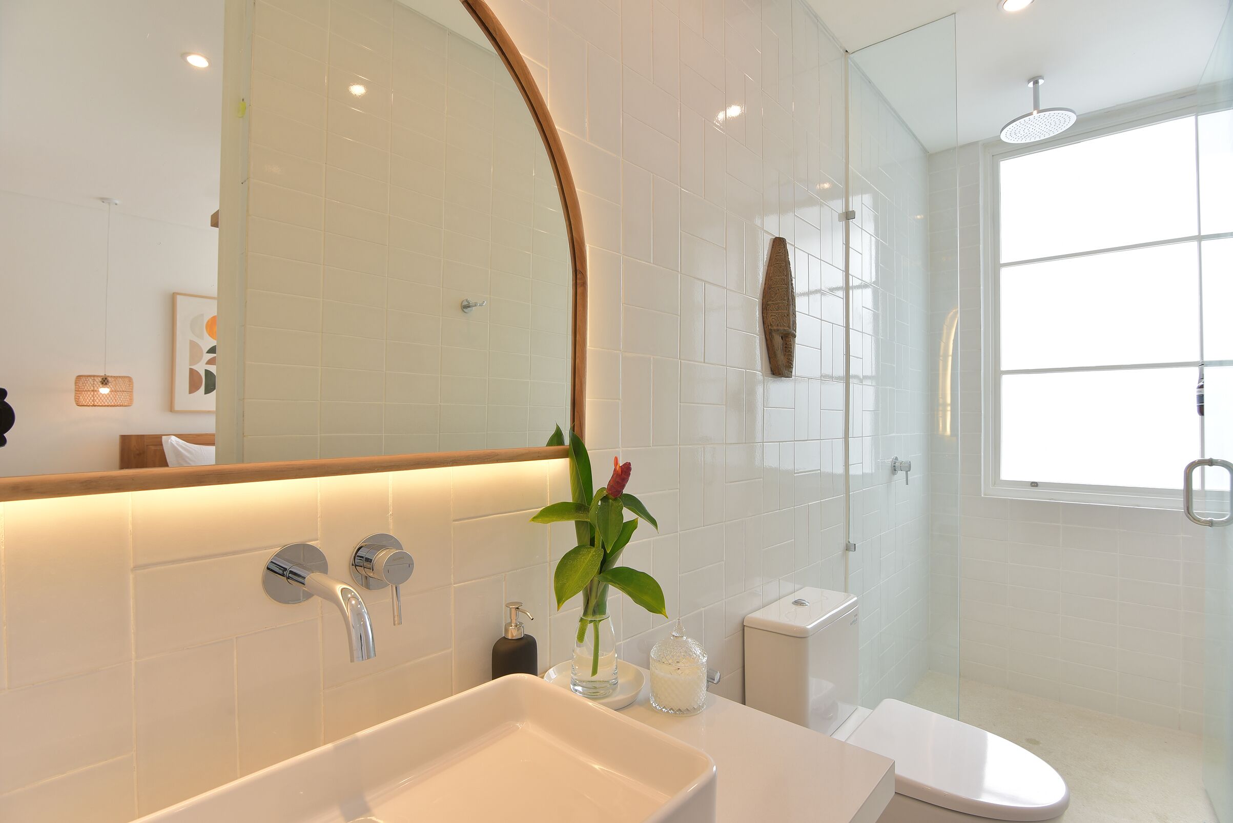 A modern bathroom with a large mirror, a white sink, a toilet, and a shower.