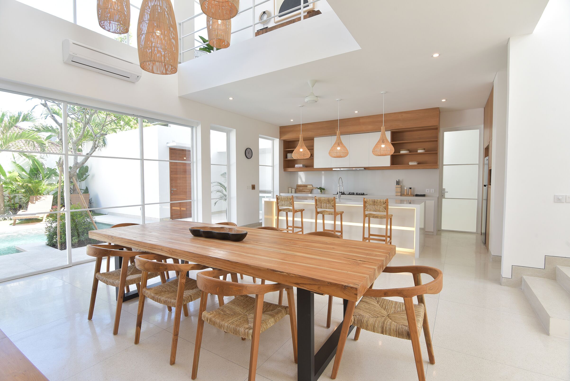 Una cocina moderna con armarios de madera, un comedor con una mesa grande y sillas, y vista a una piscina.