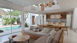 A modern living room with a large sofa, a wooden coffee table, and a dining area with a wooden table and hanging pendant lights. - Villa Cruz in the centre Berawa (Canggu)