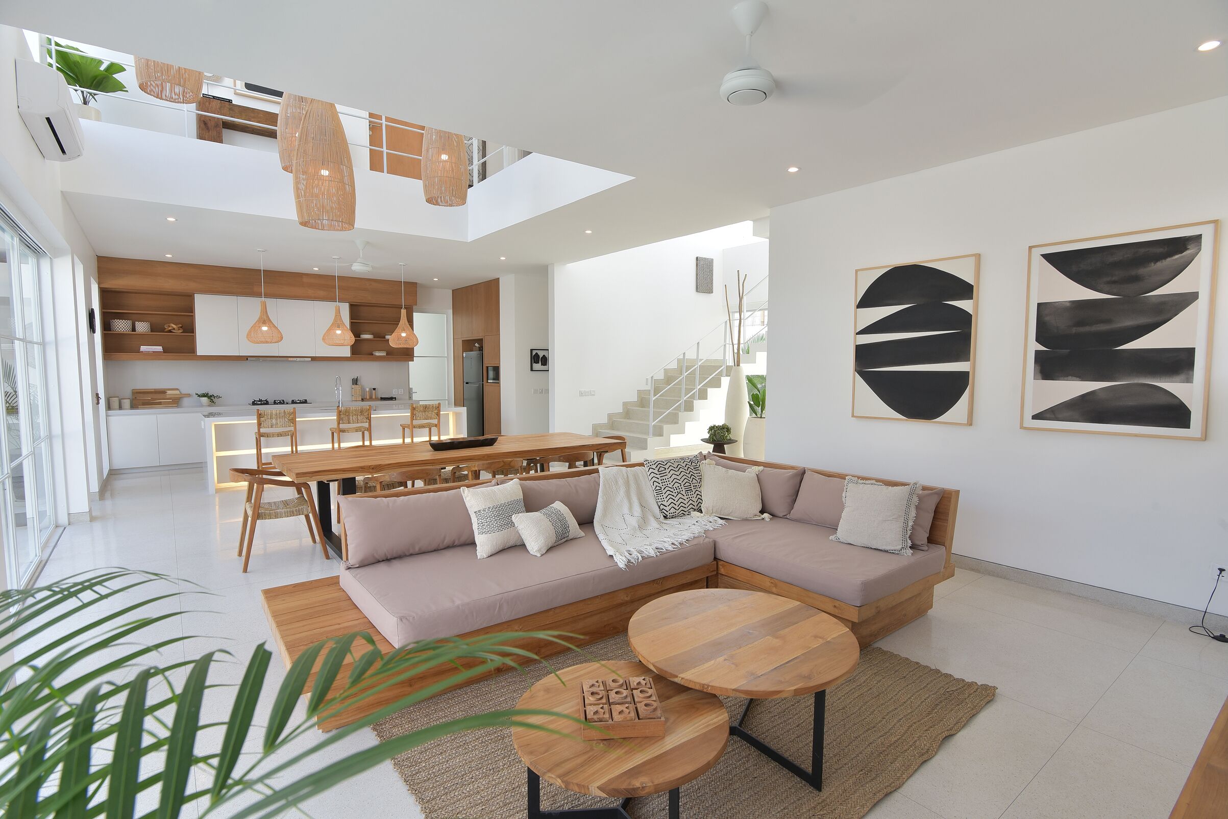 Un espace de vie moderne comprenant un canapé d’angle, des tables basses rondes et un coin repas avec une table et des chaises en bois.