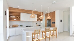 A modern kitchen with white cabinetry, a central island with bar stools, and pendant lighting. - Villa Cruz in the centre Berawa (Canggu)