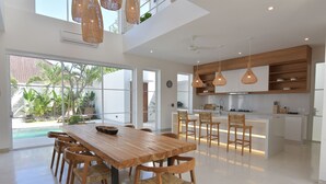 A spacious kitchen with a central island, wooden chairs, and pendant lighting. - Villa Cruz in the centre Berawa (Canggu)