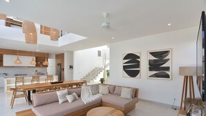 A modern living room with a sectional sofa, a round wooden coffee table, and a dining area with a wooden table and chairs. - Villa Cruz in the centre Berawa (Canggu)