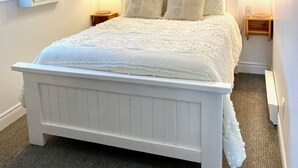 Een slaapkamer met een wit bed, twee nachtkastjes met lampen, een houten balk in het plafond en een witte muur met een verlichtingsarmatuur.