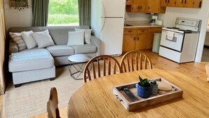 Een gezellige keuken met houten kastjes, een witte koelkast en een fornuis. Er staat een eettafel met stoelen en een klein bijzettafeltje.