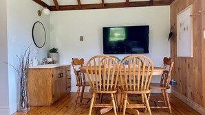 Een eethoek met een houten tafel en stoelen, een televisie aan de muur en een houten kast met een wastafel.