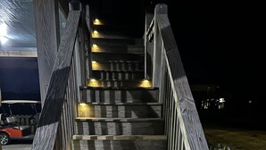 Eine hölzerne Treppe mit Geländern und Beleuchtung, die zu einer oberen Ebene führt.