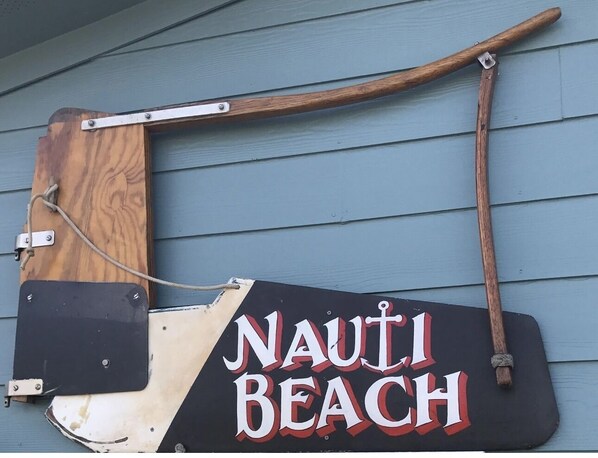 Une enseigne en bois portant l’inscription « NAUTI BEACH » est fixée à une maison.