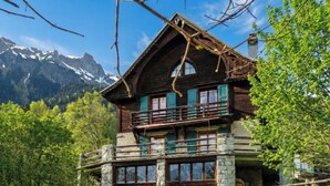 A wooden chalet with a balcony, stone foundation, and a mountain backdrop. - Grand Chalet des Moussoux 6BR: Terrace, Garden, Views, Sleeps 10, Chamonix, France (Chamonix)