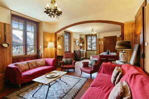 A cozy living room with a fireplace, red sofas, and a view of snow-capped mountains through large windows.