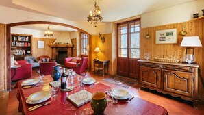 A dining area with a wooden table set for a meal, a fireplace, and a bookshelf. - Grand Chalet des Moussoux 6BR: Terrace, Garden, Views, Sleeps 10, Chamonix, France (Chamonix)