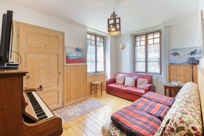 Una habitación acogedora con un piano de madera, un sofá rojo y un sofá floral.