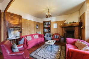 Una sala de estar acogedora con chimenea, sofás de cuero, una estantería y un candelabro.