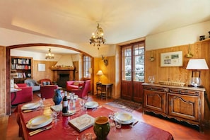 A dining area with a wooden table set for four, a fireplace, and a bookshelf in the background.
