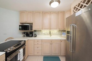 Une cuisine avec des meubles de couleur bois clair, un réfrigérateur en acier inoxydable, un four à micro-ondes, une cuisinière et un évier.