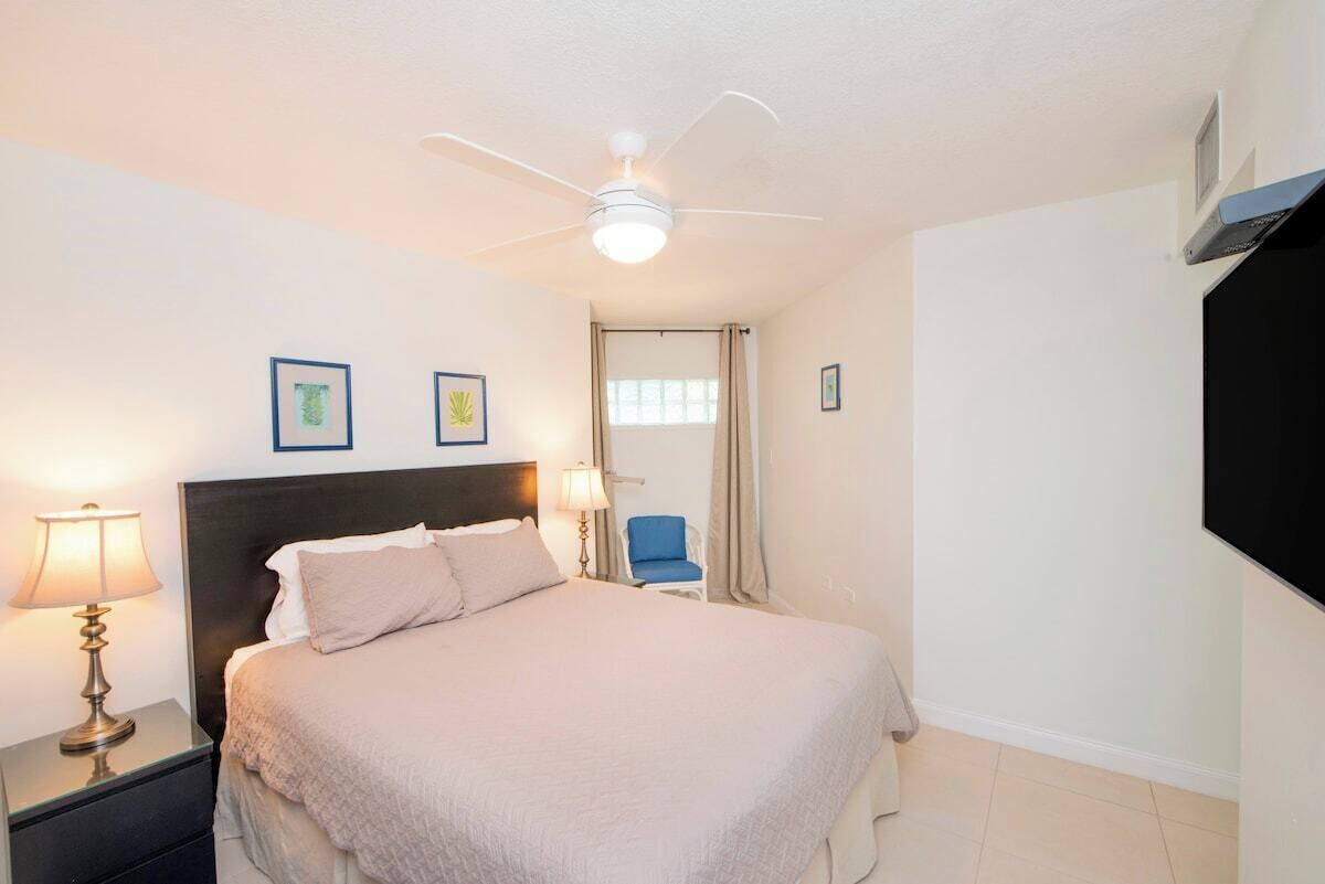 A hotel room with a bed, nightstand, lamp, ceiling fan, and a chair.